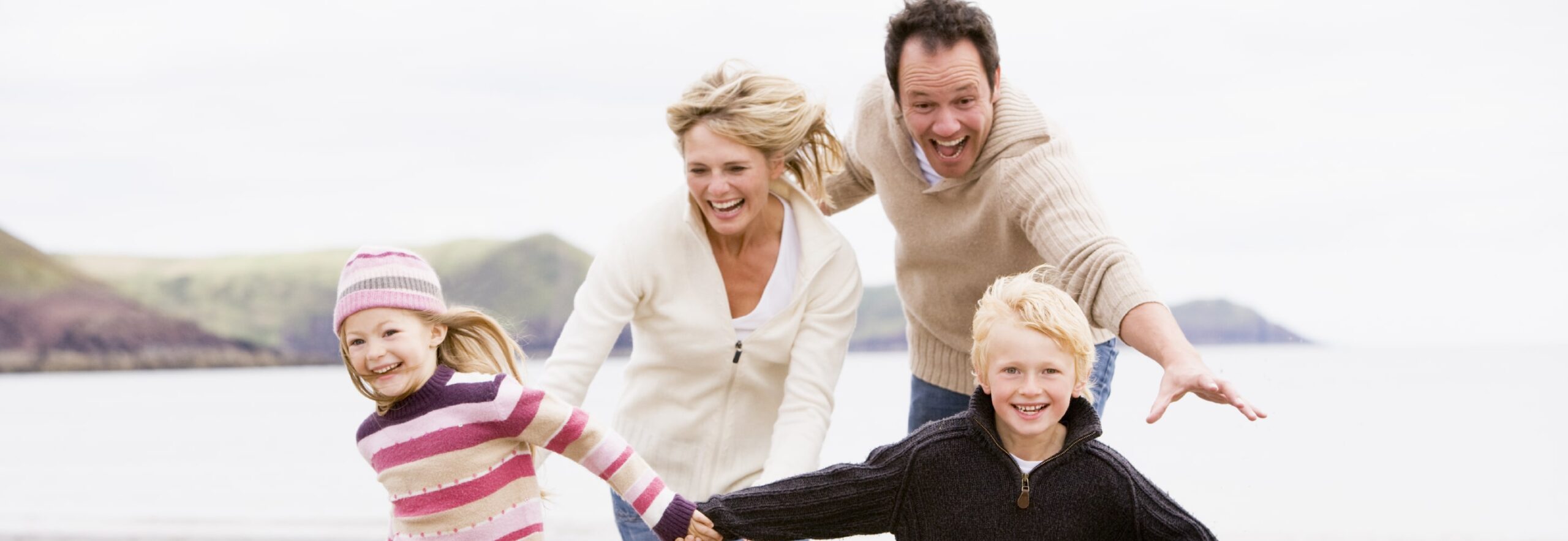 Family running on beach holding hands smiling