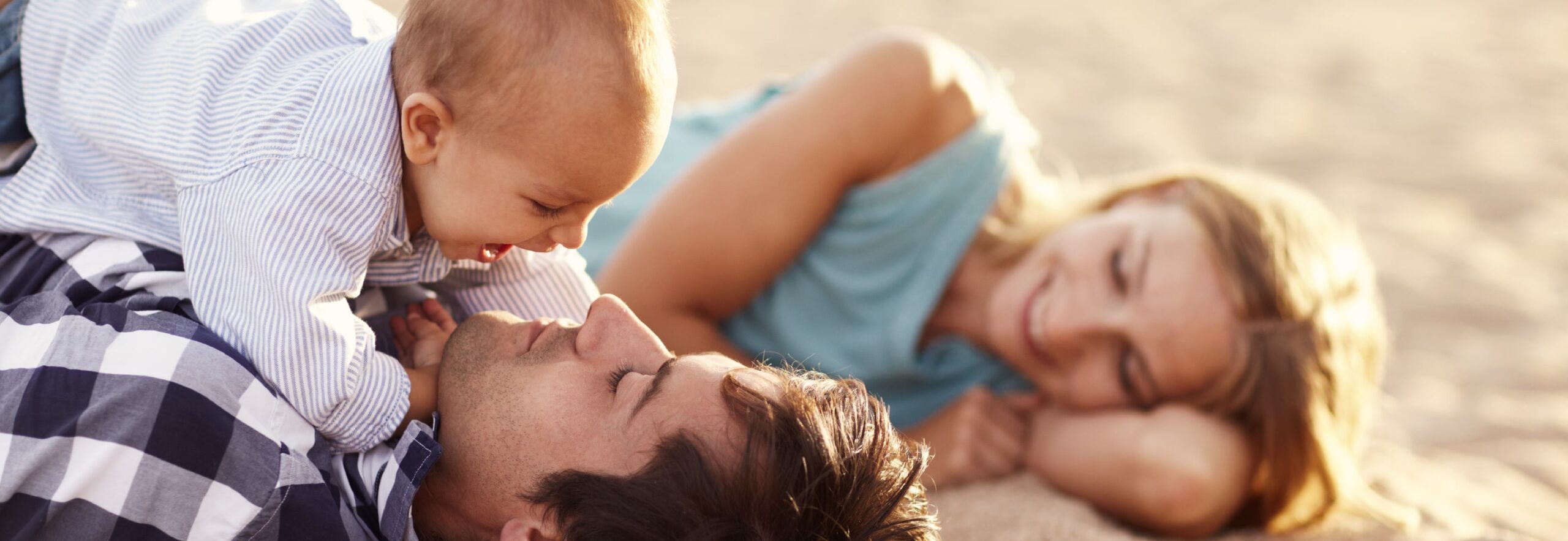 Baby boy playing with his dad on the beach, mum smiling in the background