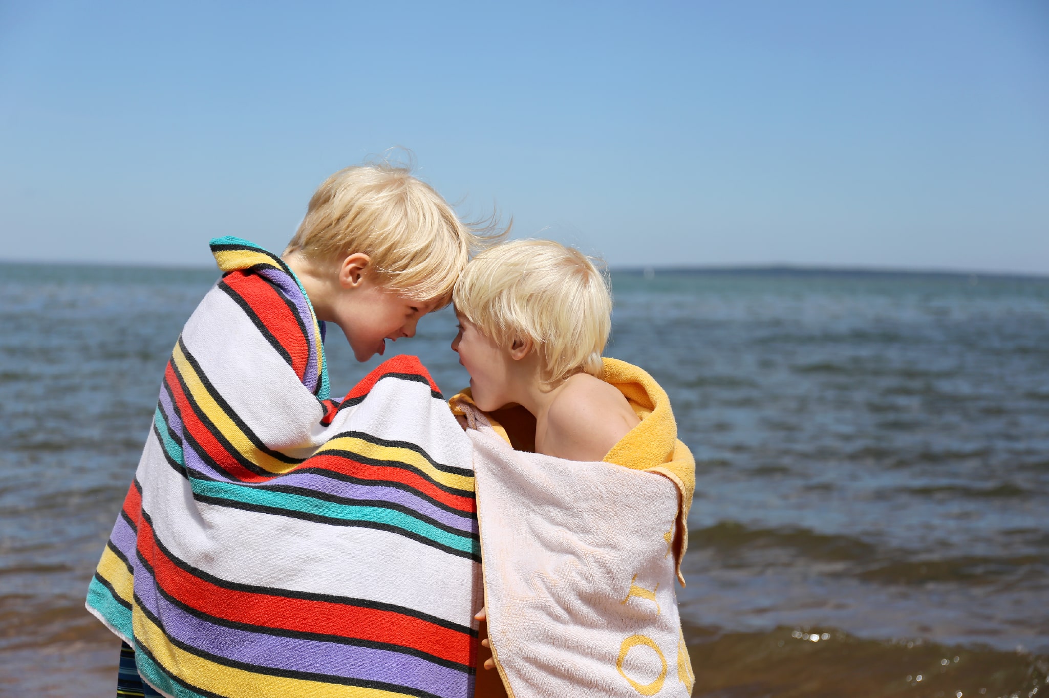 Two blonde boys playing in beach towels near the sea
