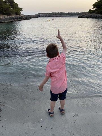 6 year old boy in pink shirt throwing rock into sea