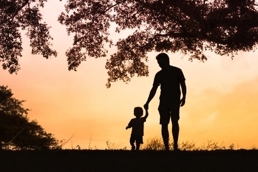 Silhouette of dad with young son next to a tree 